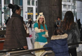 Dressed for Mardi Gras, young drug prevention volunteer hands out drug education booklets to a child at a train station in the heart of Brussels, Belgium.